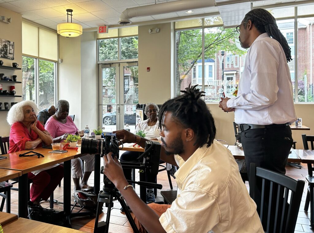 story circle participants sit around tables while one gentleman is standing and speakin