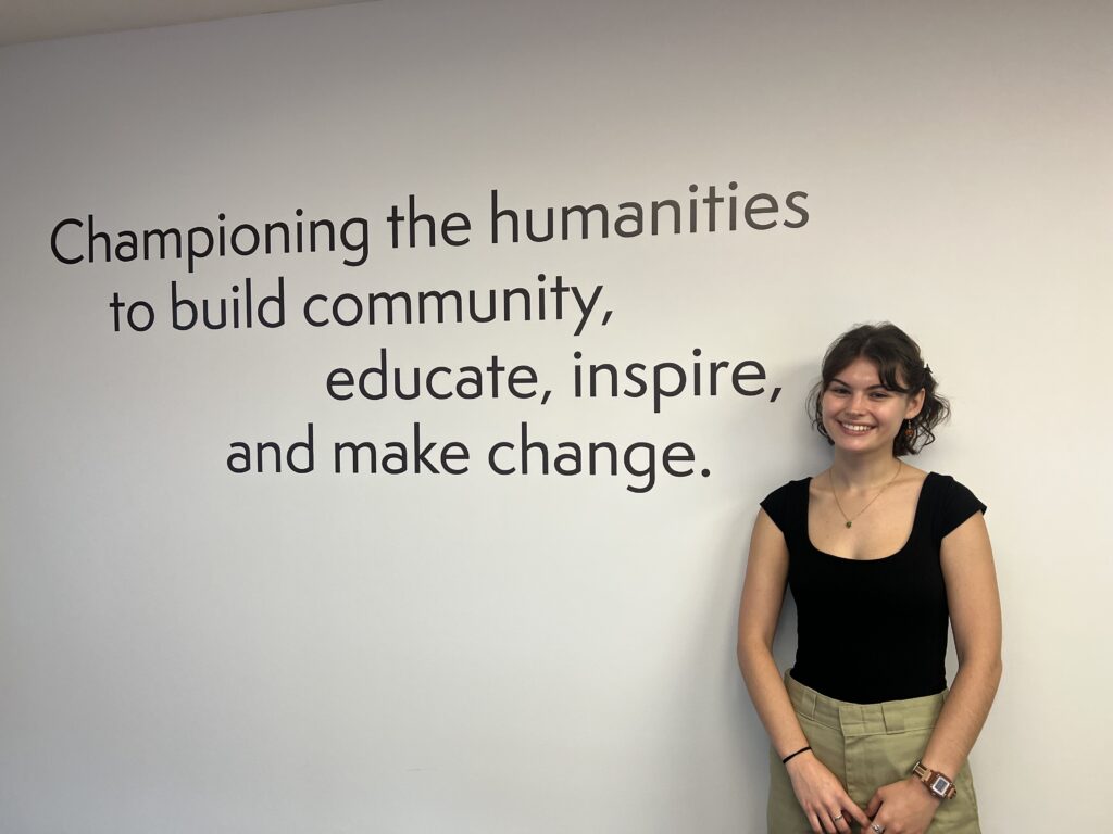 Intern Maia Schwallie poses next to an inscription about the power of the humanities at the PA Humanities office.