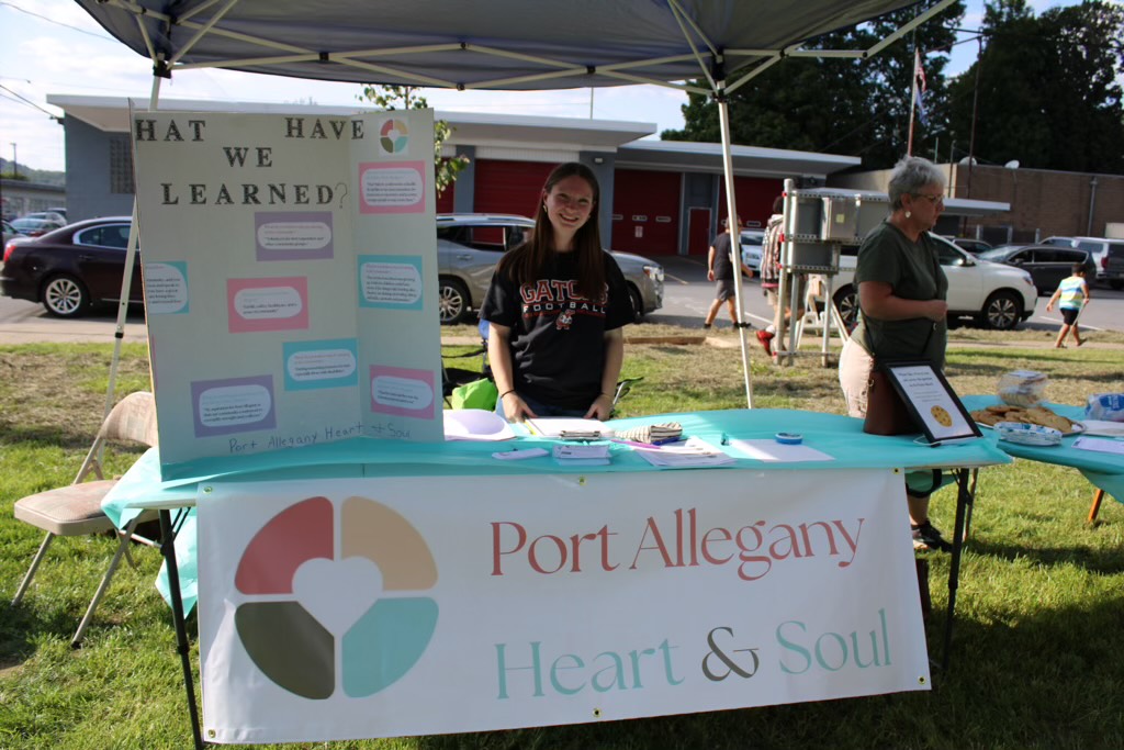 Allie O'Shea stands behind a table that the Port Allegany Heart & Soul team set up outside during a community event this summer to gather stories from residents about what they love about their community.