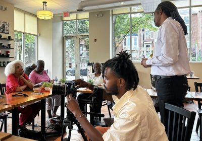 story circle participants sit around tables while one gentleman is standing and speakin