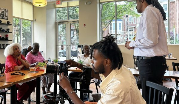 story circle participants sit around tables while one gentleman is standing and speakin