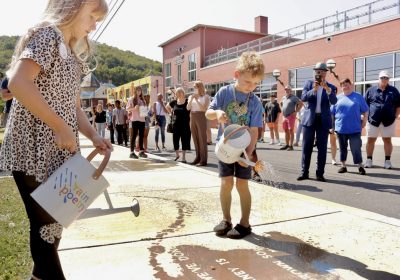 a young boy and girl use watering cans to sprinkle water on the sidewalk, making poetry appear like magic when the pavement gets wet