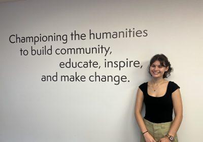 Intern Maia Schwallie poses next to an inscription about the power of the humanities at the PA Humanities office.