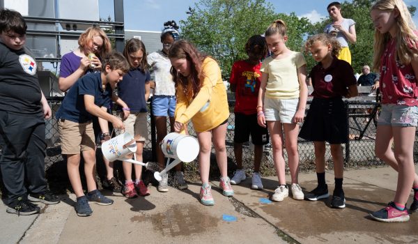 Students from Assemble pour water over the sidewalk to make their invisible words appear like magic at the Rain Poetry reveal celebration at Nelson Mandela Peace Park in Pittsburgh's Garfield neighborhood.    Photo by Joe Appel.