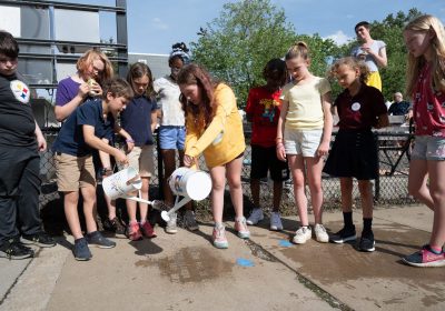 Students from Assemble pour water over the sidewalk to make their invisible words appear like magic at the Rain Poetry reveal celebration at Nelson Mandela Peace Park in Pittsburgh's Garfield neighborhood.    Photo by Joe Appel.